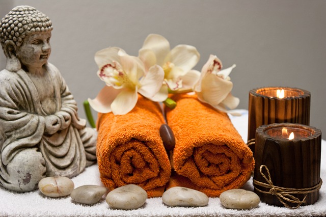 2 serviettes enroulées sur une table avec un Bouddha, des pierres , deux bougies et des fleurs